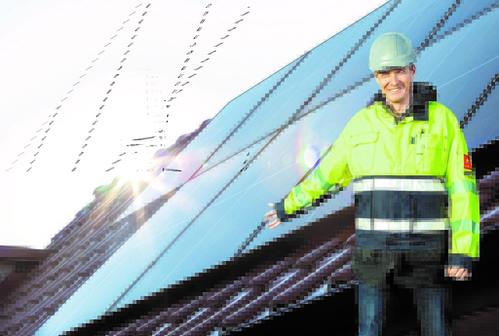 En man i varseljacka står framför ett tak med solceller.