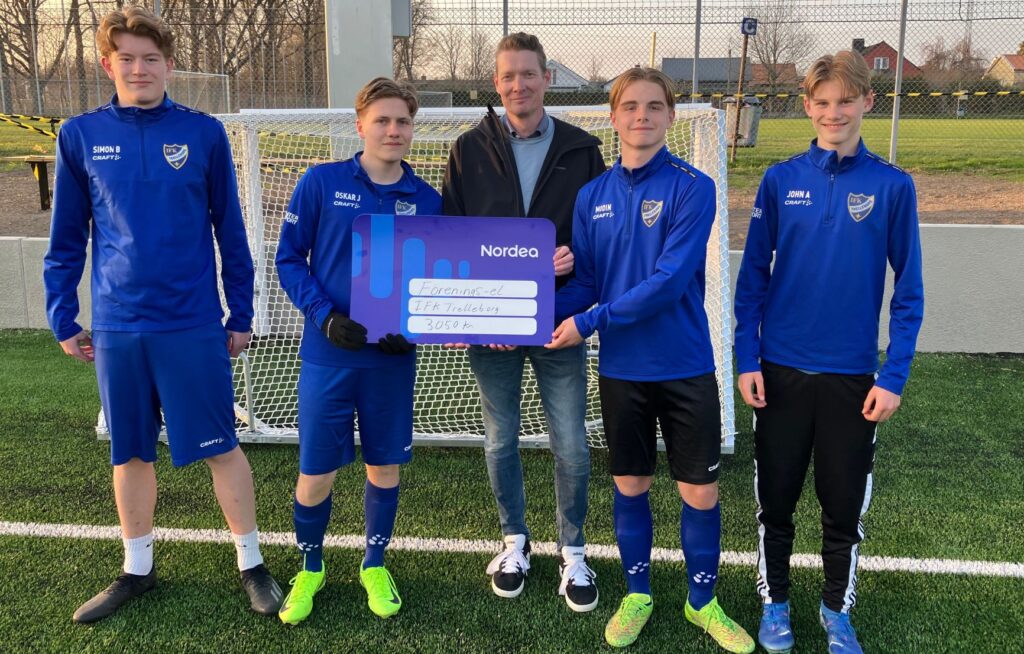 Fyra ungdomsspelare från IFK Trelleborg FK visar upp en symbolisk check med texten "Förenings-el, IFK Trelleborg, 3 050 kr" på en konstgräsplan, tillsammans med en representant från Trelleborgs Energi.