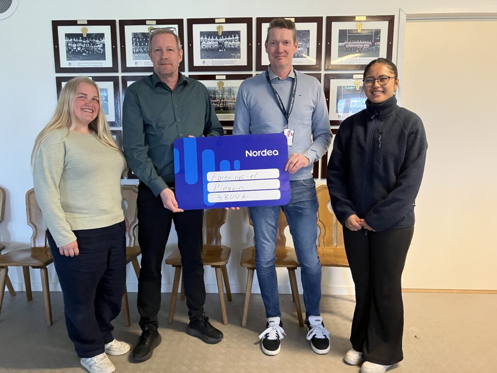 Representanter från Pingvin RC visar upp en symbolisk check med texten 'Förenings-el, Pingvin, 3 800 kr' inomhus, tillsammans med en representant från Trelleborgs Energi.